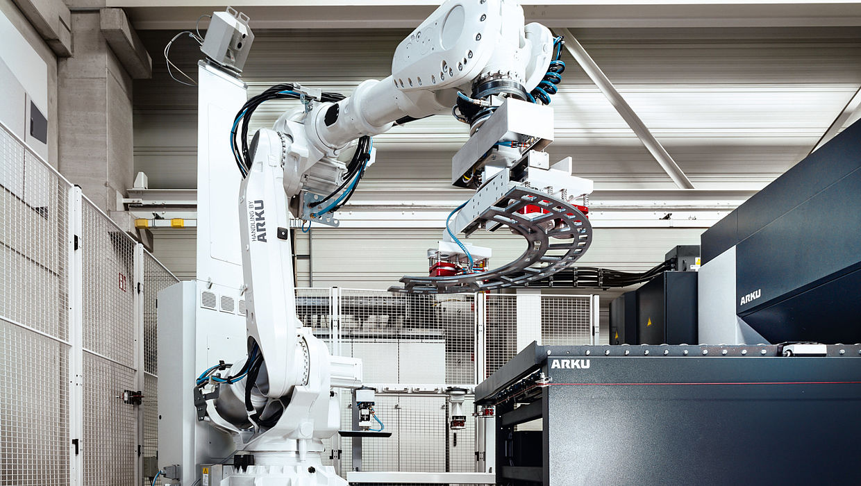 Handling robot lifts part onto conveyor belt of leveler.