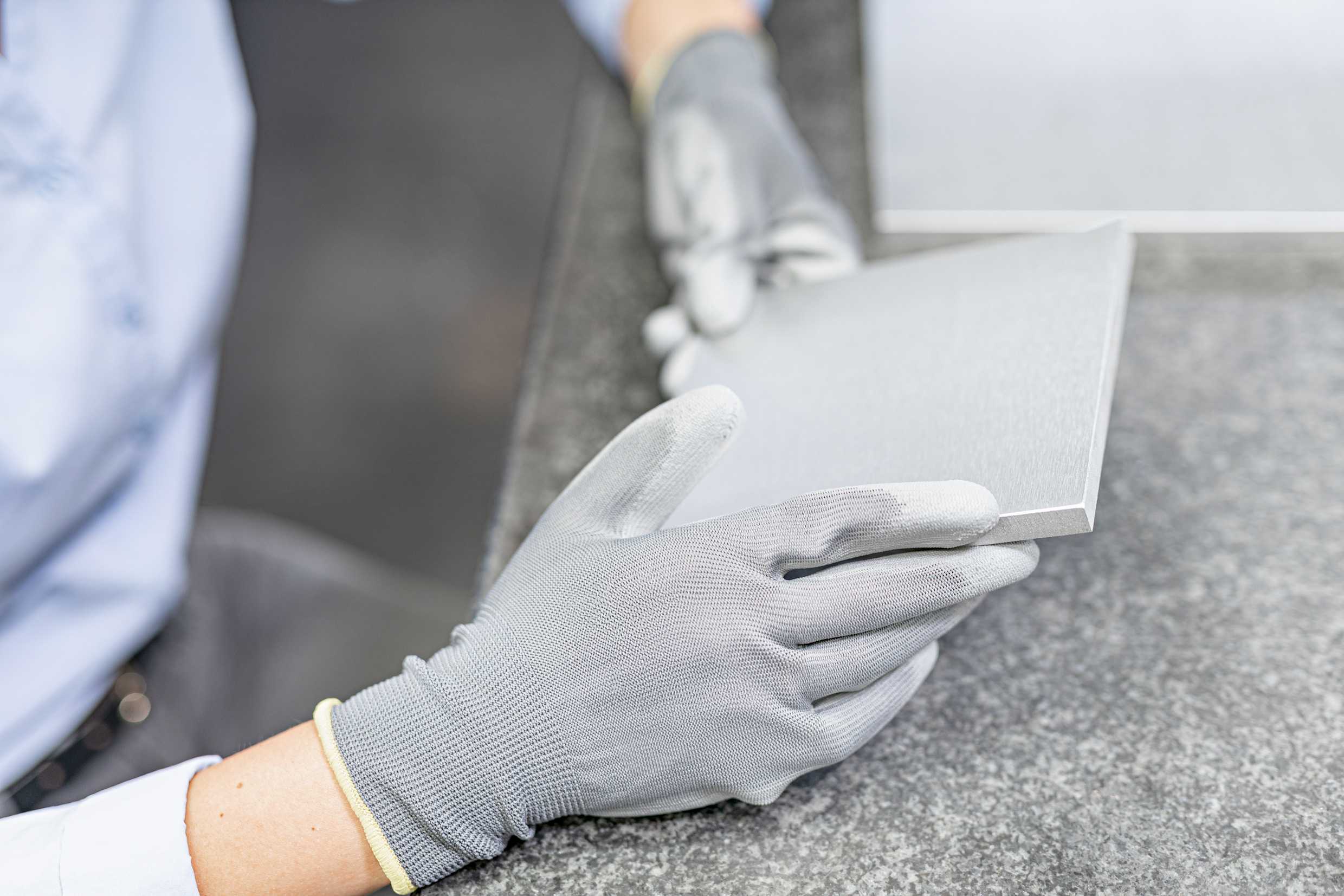 Hände mit Handschuhen halten ein dickes Blech, das vom ARKU EdgeBreaker 3000 NEXT entgratet wurde